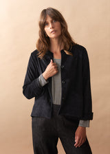 Woman wearing a black corduroy jacket over a striped shirt against a beige background