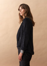 Woman wearing a dark black corduroy jacket against a beige background