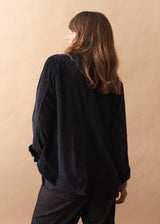 Person wearing a black corduroy oversized jacket against a beige background