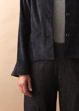 Person wearing a black corduroy jacket over a striped shirt with a beige background