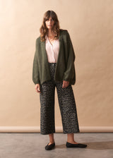 Woman wearing a green cardigan, white shirt, and patterned pants against a beige background