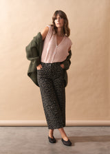 Woman wearing a pink top, green cardigan, and patterned pants against a beige wall.