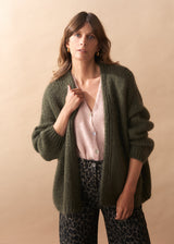 Woman wearing a green cardigan over a pink top and leopard print pants on a beige background