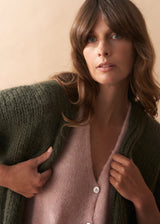 Woman wearing a green cardigan over a pink top against a beige background