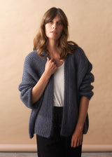 Woman wearing a slate grey chunky knitted cardigan against a beige background