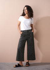 Woman wearing a white t-shirt and khaki leopard print wide leg trousers against a beige background