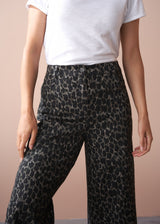 Person wearing a white t-shirt and khaki leopard print wide leg trousers on a beige background