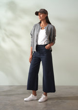 Woman wearing a gray cardigan, white shirt, navy wide leg trousers, and white sneakers against a plain background