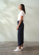 Woman wearing a white top and navy wide leg trousers standing against a plain background