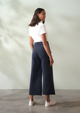 Woman wearing a white shirt and navy wide leg trousers against a plain background