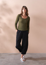 Woman wearing a green cashmere blend top and black trousers against a beige background
