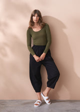 Woman wearing a green cashmere blend top and black pants against a beige wall.
