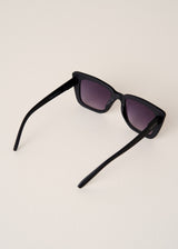 Black sunglasses with purple lenses on a light beige background