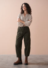Woman wearing a patterned cotton blouse and green barrel leg trousers against a beige background