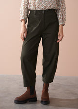 Woman wearing a patterned cotton blouse and green barrel leg trousers against a beige background