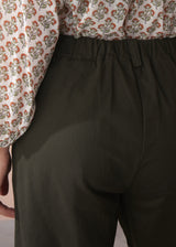 Woman wearing a patterned cotton blouse and green barrel leg trousers against a beige background