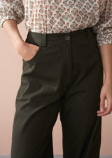Woman wearing a patterned cotton blouse and green barrel leg trousers against a beige background