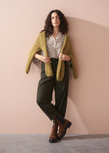 Woman wearing a patterned cotton blouse and green barrel leg trousers against a beige background