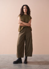 Woman wearing a green sleeveless top and wide-leg cargo trousers against a beige background