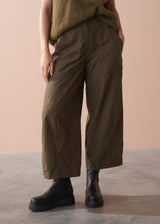 Woman wearing a green sleeveless top and wide-leg cargo trousers against a beige background