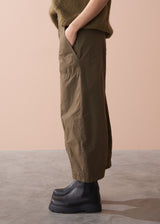 Woman wearing a green sleeveless top and wide-leg cargo trousers against a beige background