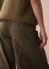 Person wearing a brown knitted sweater and matching pants against a beige background