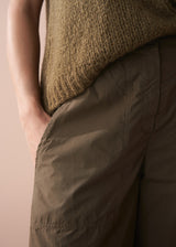 Person wearing a brown knitted sweater and dark green pants against a beige background