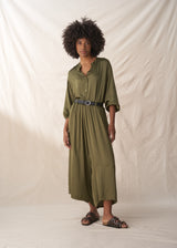 Woman wearing an olive green shirt and trousers with a belt against a plain background