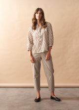 Woman wearing a floral blouse and beige pants against a beige background