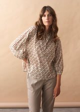 Woman wearing a floral blouse and beige pants against a beige background