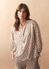 Woman wearing a floral blouse and beige pants against a beige background