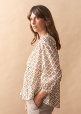 Woman wearing a floral blouse and beige pants against a beige background