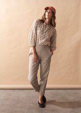 Woman wearing a patterned v-neck blouse with beige trousers and black shoes
