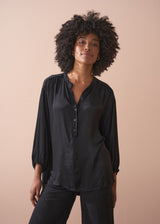 Woman wearing a black satin blouse and black wide leg trousers against a beige background