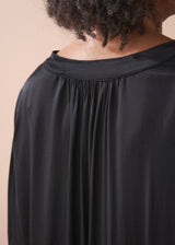 Woman wearing a black satin blouse and black wide leg trousers against a beige background