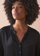 Woman wearing a black satin blouse and black wide leg trousers against a beige background