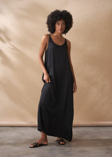 A woman in a scoop-neck black satin maxi dress stands against a beige background.