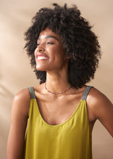 Woman with curly hair wearing a yellow satin maxi dress against a beige background