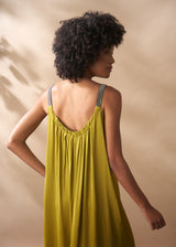 Woman wearing a yellow satin maxi dress with thin straps against a beige background