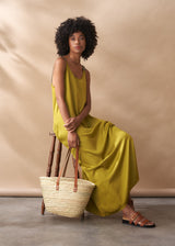 Woman in a yellow satin maxi dress sitting on a wooden stool with a woven basket against a beige background