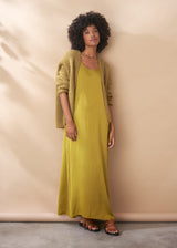 Woman wearing a long satin maxi dress dress and cardigan against a beige background