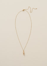 A delicate gold chain necklace with a small vertical cluster of clear stones in a gold setting, displayed against a textured off-white background.