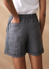 Person wearing blue checkered linen shorts on a beige background