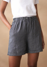 Person wearing blue and white checkered linen shorts on a beige background