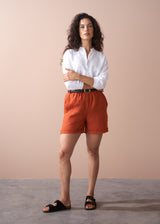 Woman wearing a white shirt and orange shorts against a beige background