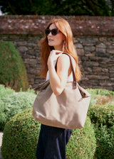 Woman wearing a beige hold all with white sleeveless top and black trousers