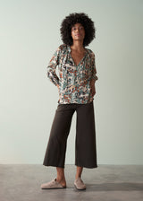 Woman wearing a floral blouse and dark pants against a plain background