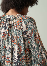 Person wearing a patterned blouse with a neutral background