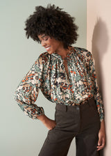 Woman wearing a floral blouse and dark pants against a light background