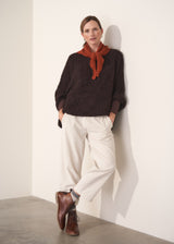 Person wearing a dark boucle sweater and cream trousers against a plain background